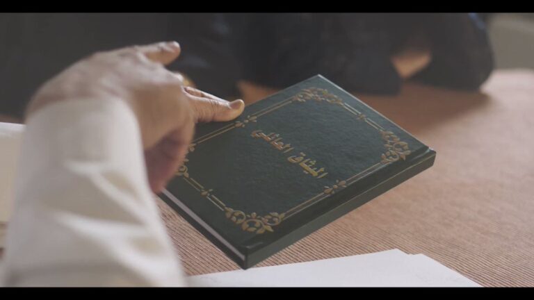 يد تمسك كتاباً بغلاف أخضر – مقال حوكمة الشركات العائلية والميثاق العائلي